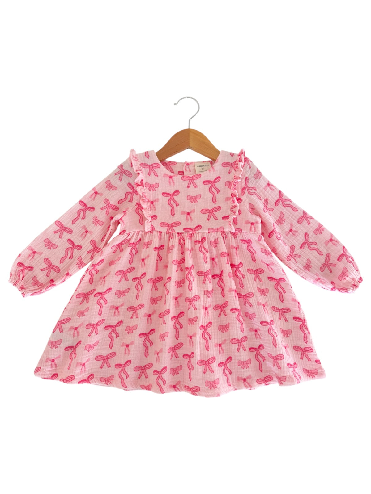 Pink long-sleeve dress with bow prints, featuring ruffled neckline and gathered waist on a wooden hanger.