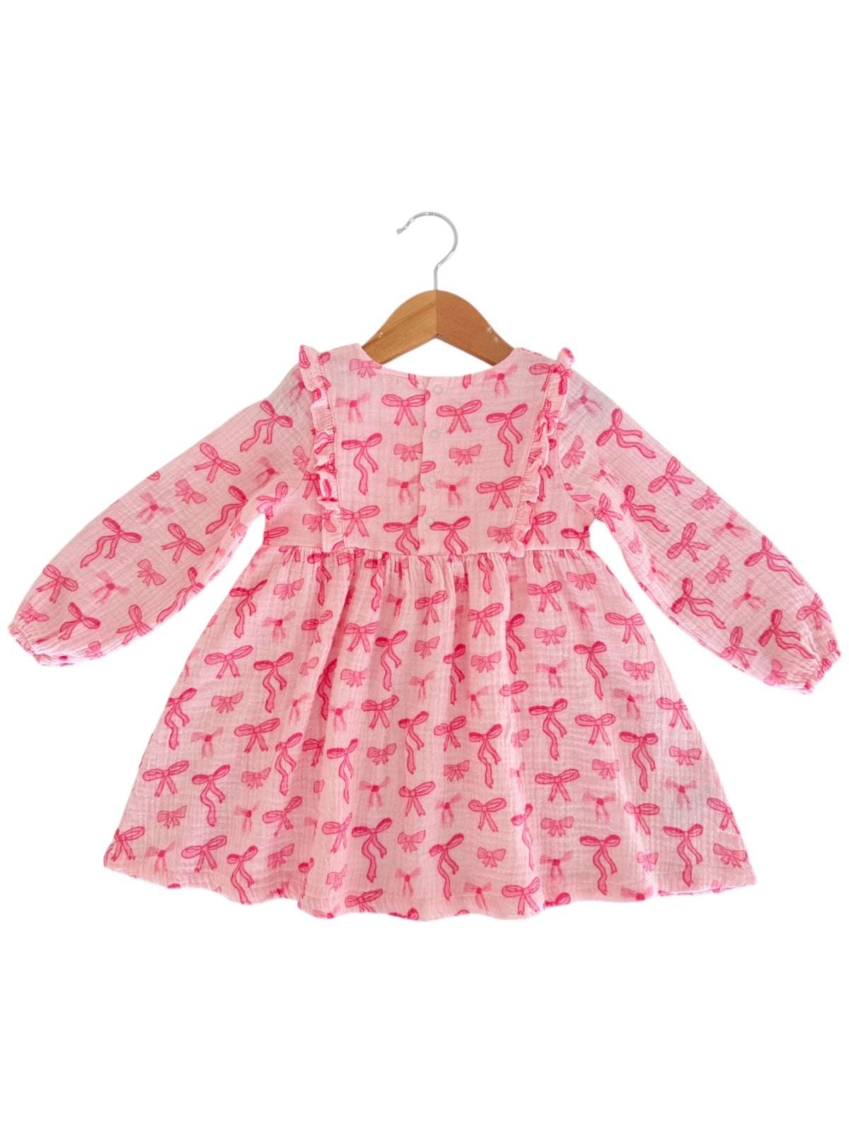 Pink dress with long sleeves and bow patterns, displayed on a hanger against a white background.