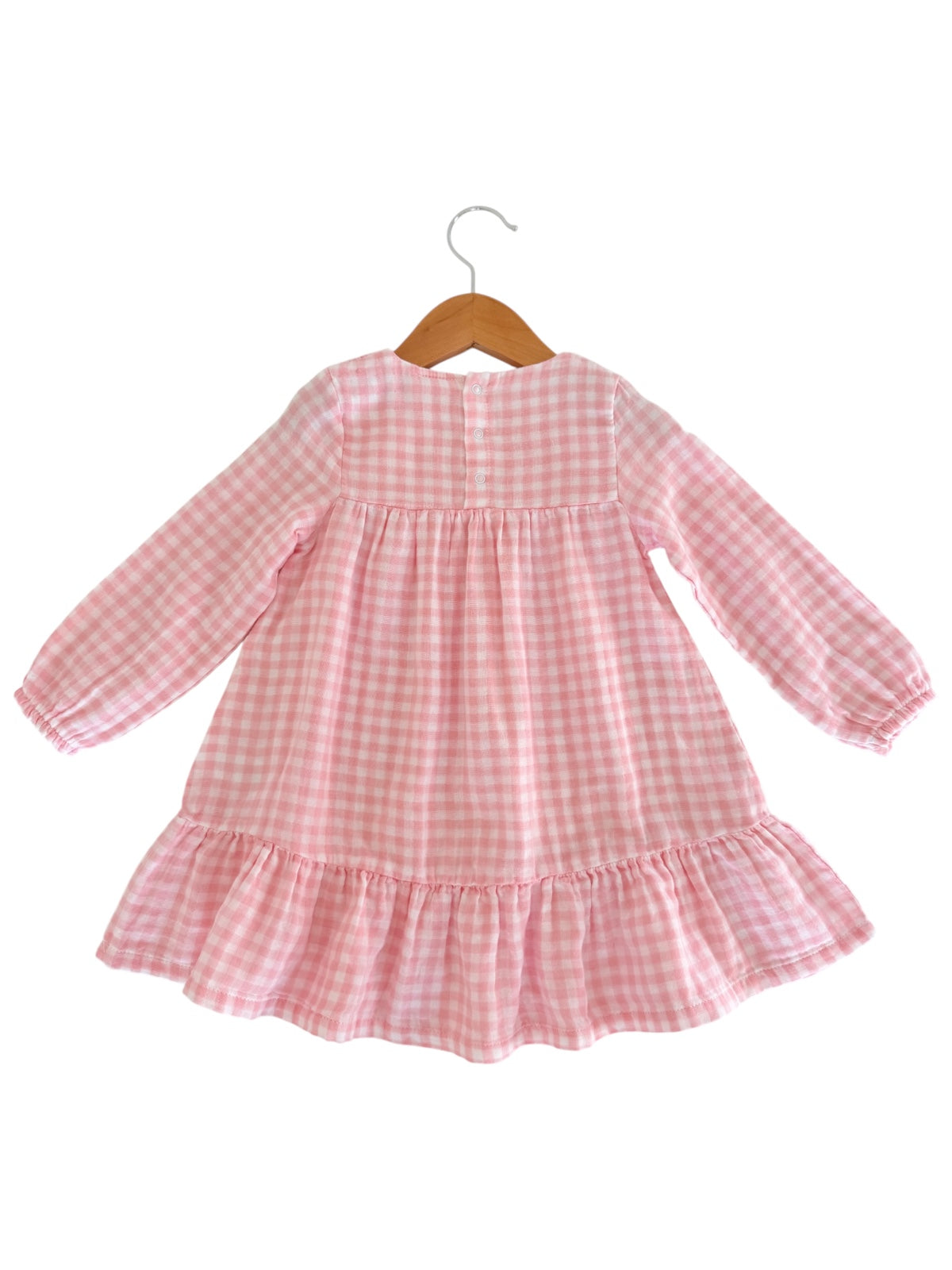 Pink gingham dress with long sleeves and ruffled hem, hanging on a wooden hanger. Back view.