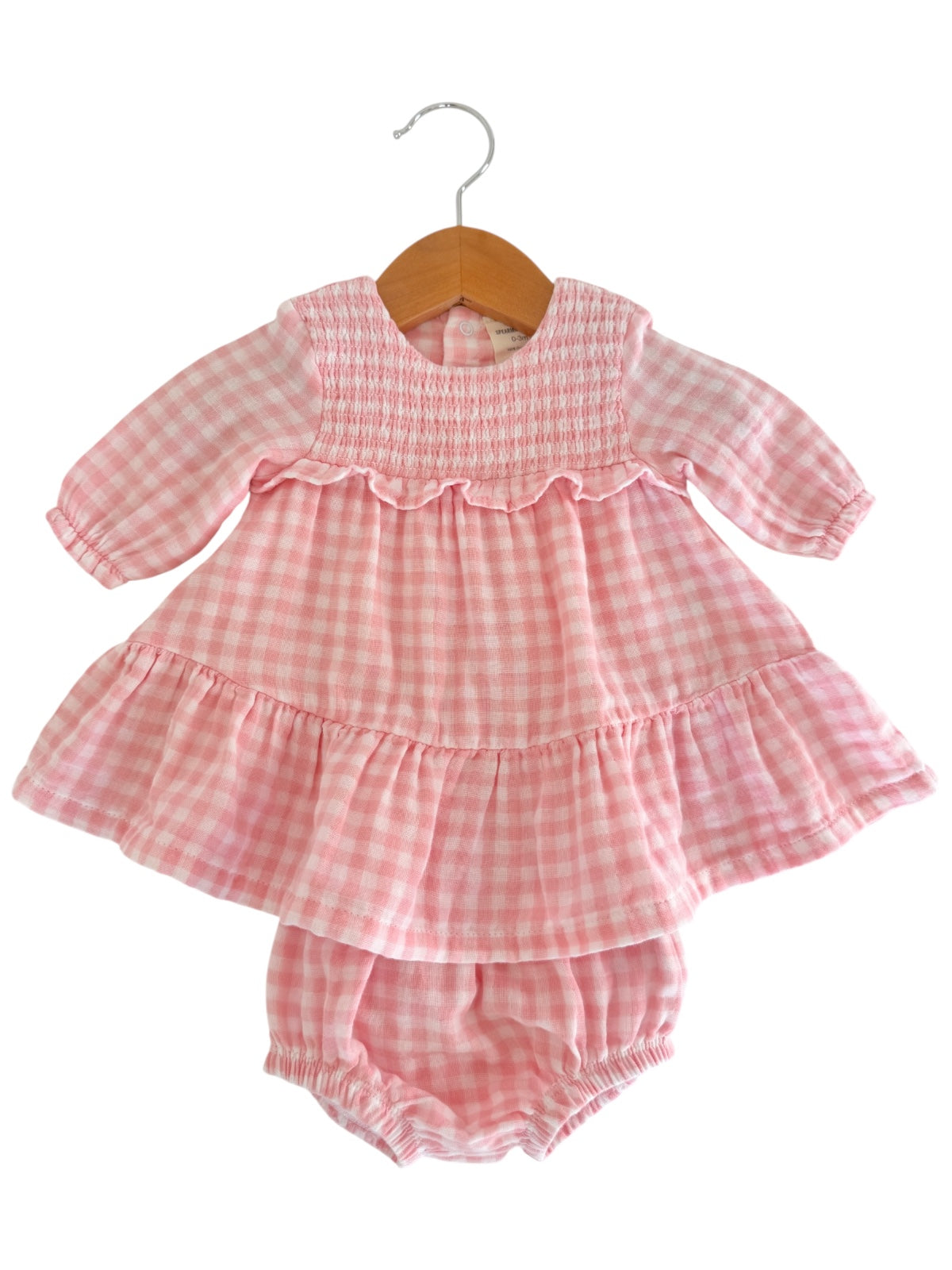 Pink gingham dress with long sleeves and ruffled hem, hung on a wooden hanger. Includes matching bloomer bottom.