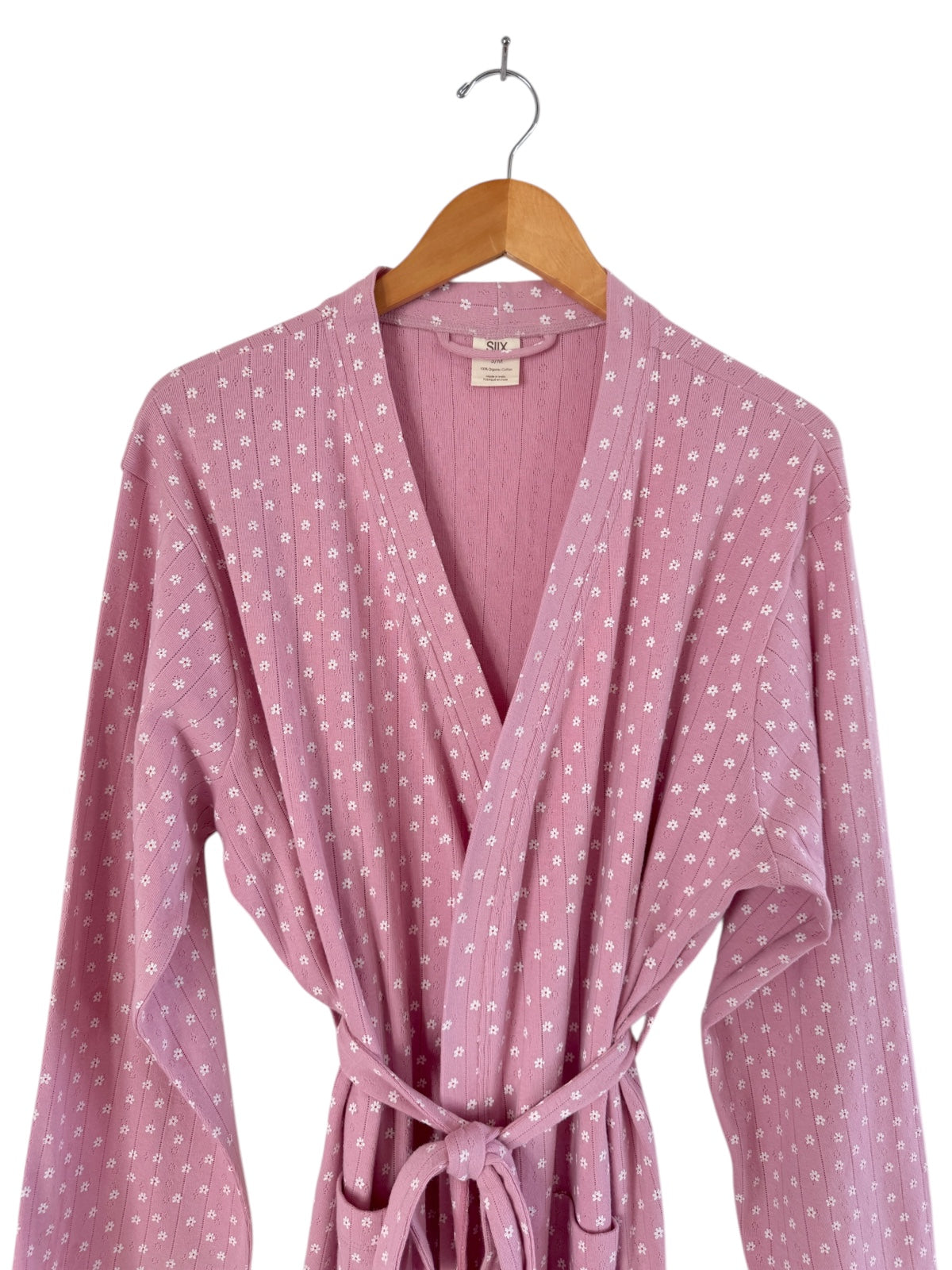 Light pink robe with white floral patterns, featuring a wrap design and a tied waist, displayed on a hanger.