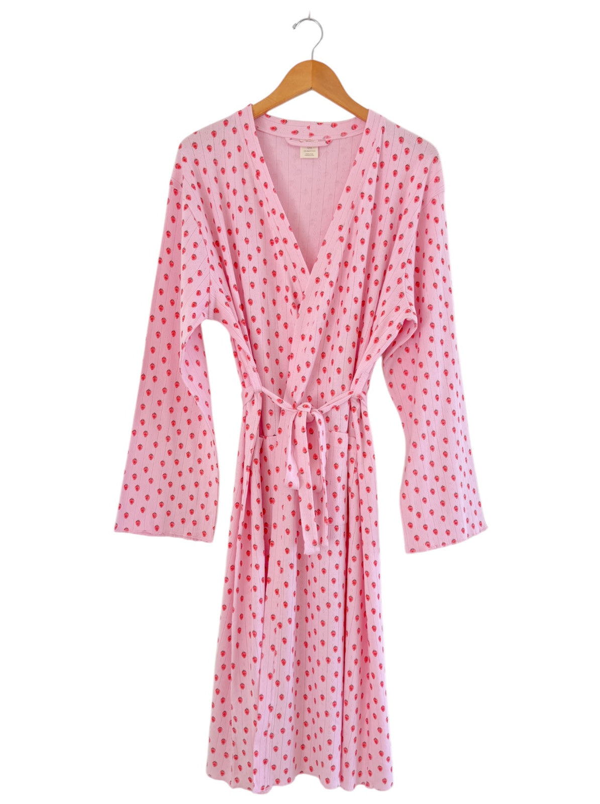 Pink robe with red polka dots, featuring long sleeves and a tied waist, hanging on a wooden hanger.