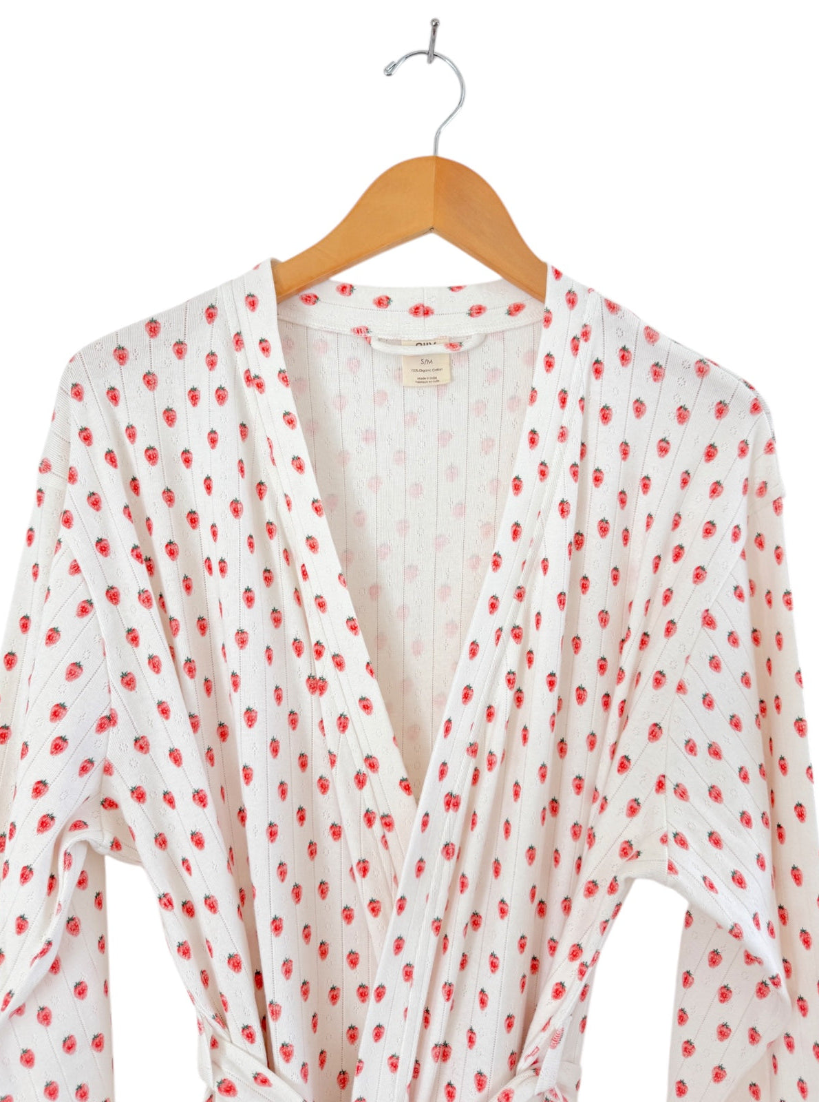 White robe covered in red strawberries, hanging on a wooden hanger against a plain background.