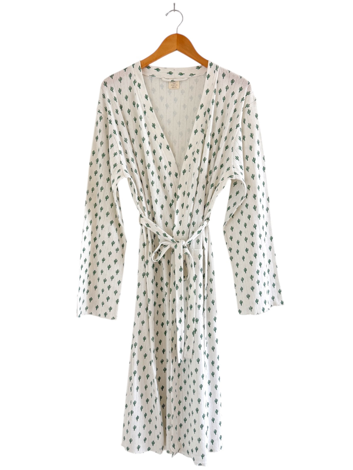White robe with green cactus pattern, hanging on a wooden hanger, featuring long sleeves and a tie waist.