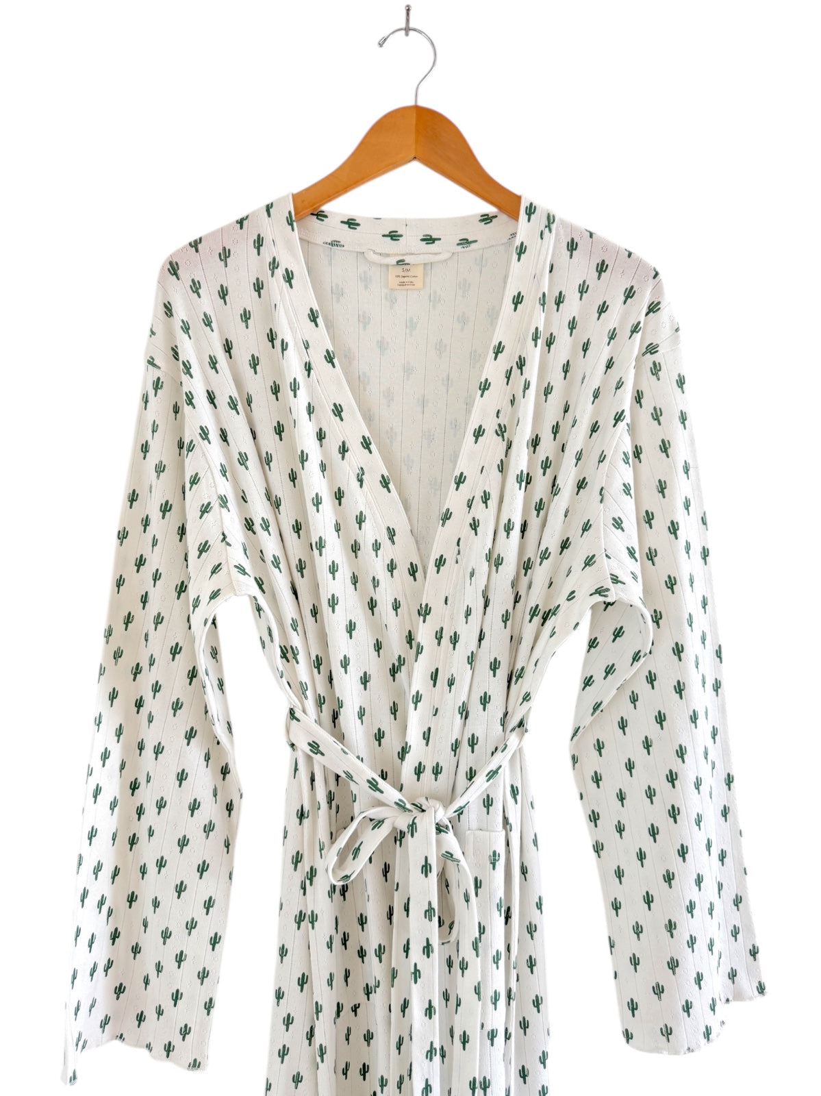 White robe with green cactus print, featuring wide sleeves and a tie waist, hanging on a wooden hanger.