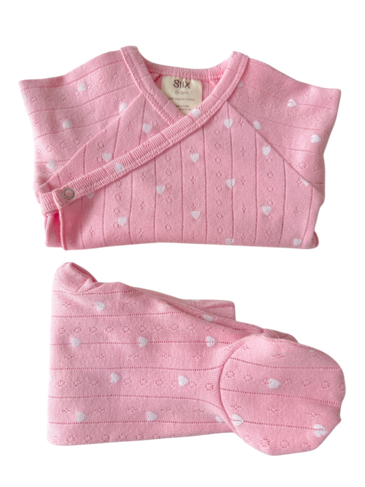 Pink baby outfit with heart patterns, including a top, pants, and hat, made from soft organic cotton.