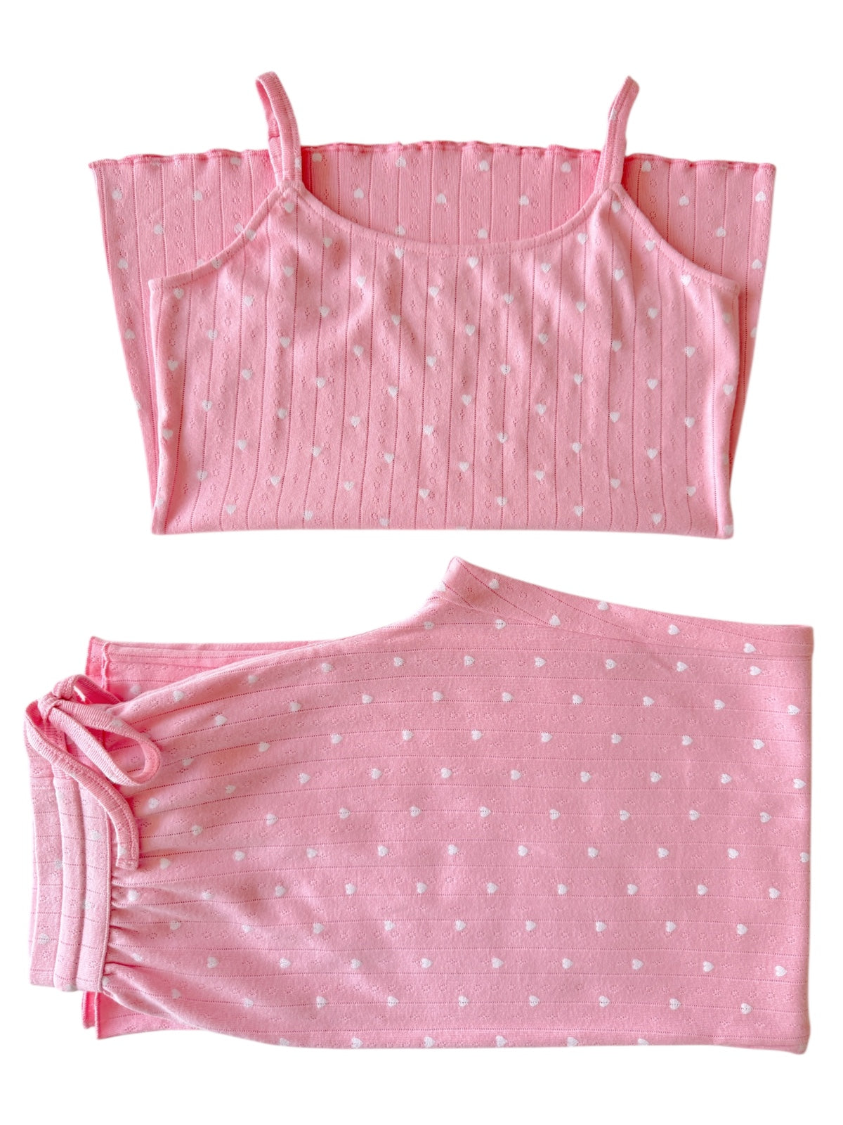 Pink pajama set featuring a spaghetti strap top and elastic waist bottoms, both with white heart patterns.