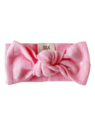 Pink headband with a knot and heart patterns, labeled with "SIIX." Ideal for stylish and comfortable wear.