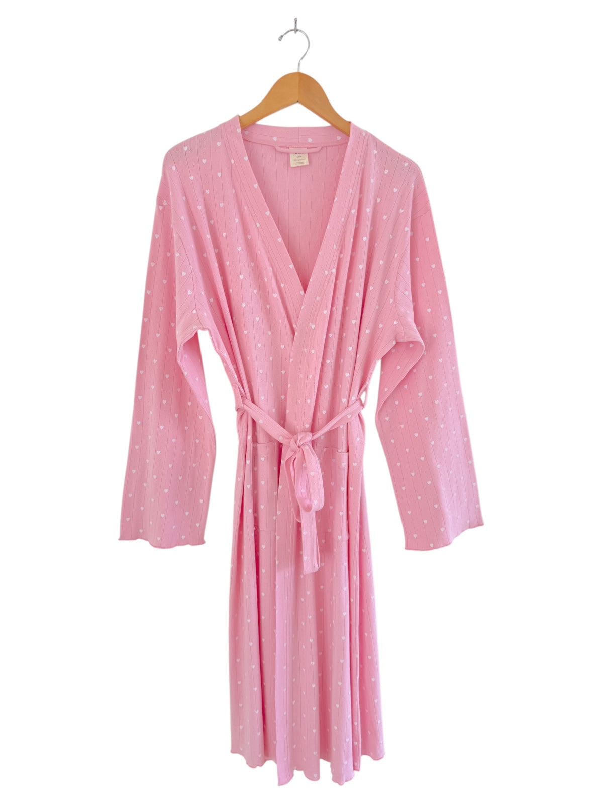 Pink robe with white polka dots hanging on a hook, featuring long sleeves and a tied waist.