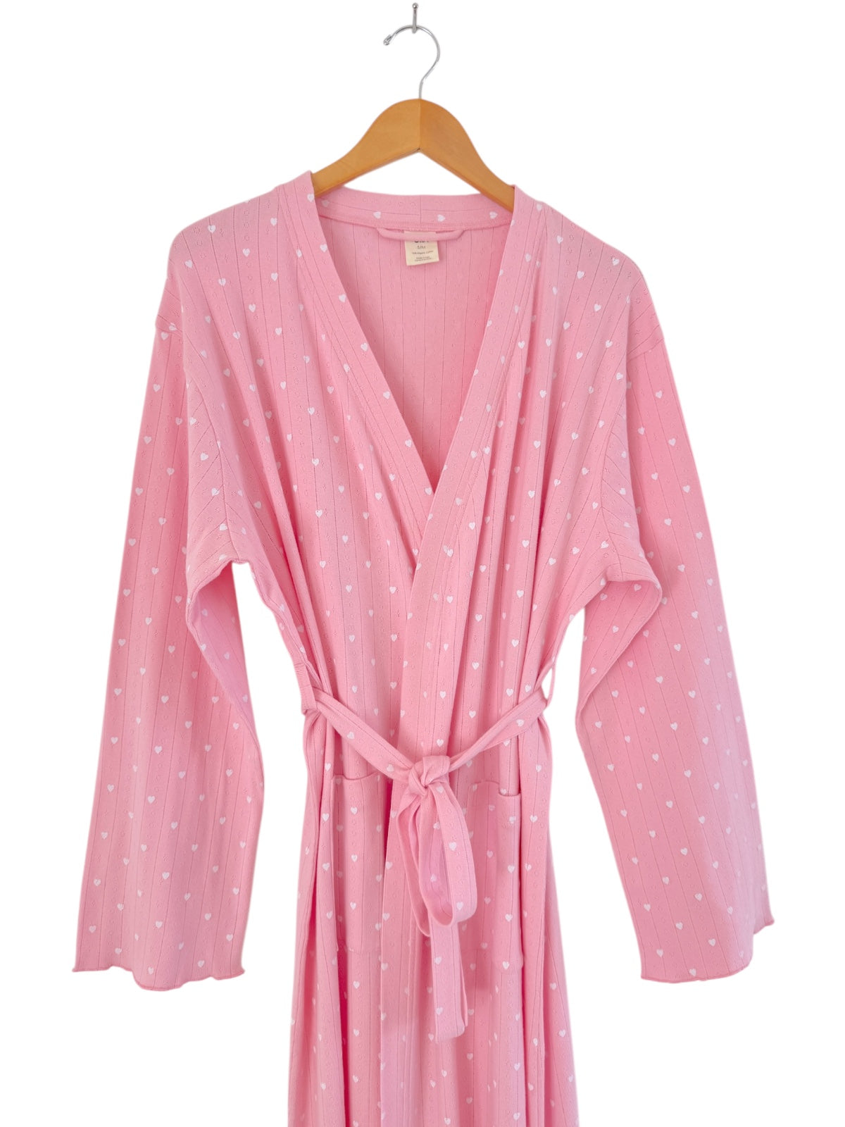 Pink robe with white hearts, tied at the waist, hanging on a wooden hanger.