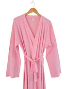 Pink robe with white hearts, tied at the waist, hanging on a wooden hanger.