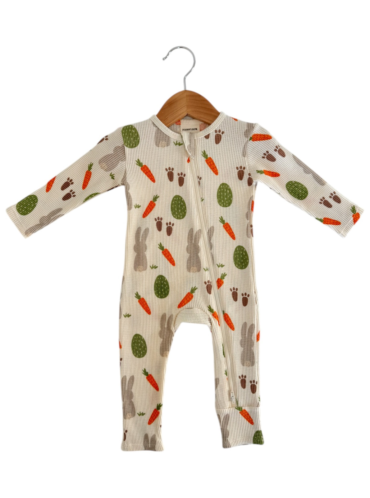 Baby onesie with bunny, carrot, and egg pattern on a light background, hanging on a wooden hanger.