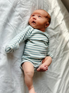Infant in a striped onesie lying on a white surface, looking up with wide eyes.
