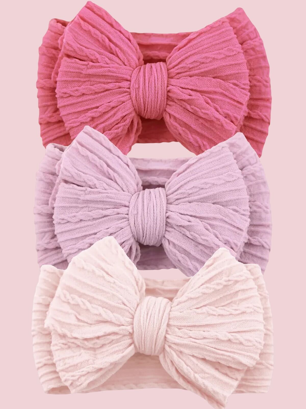 Three textured hair bows in pink, lavender, and light pink against a soft pink background.
