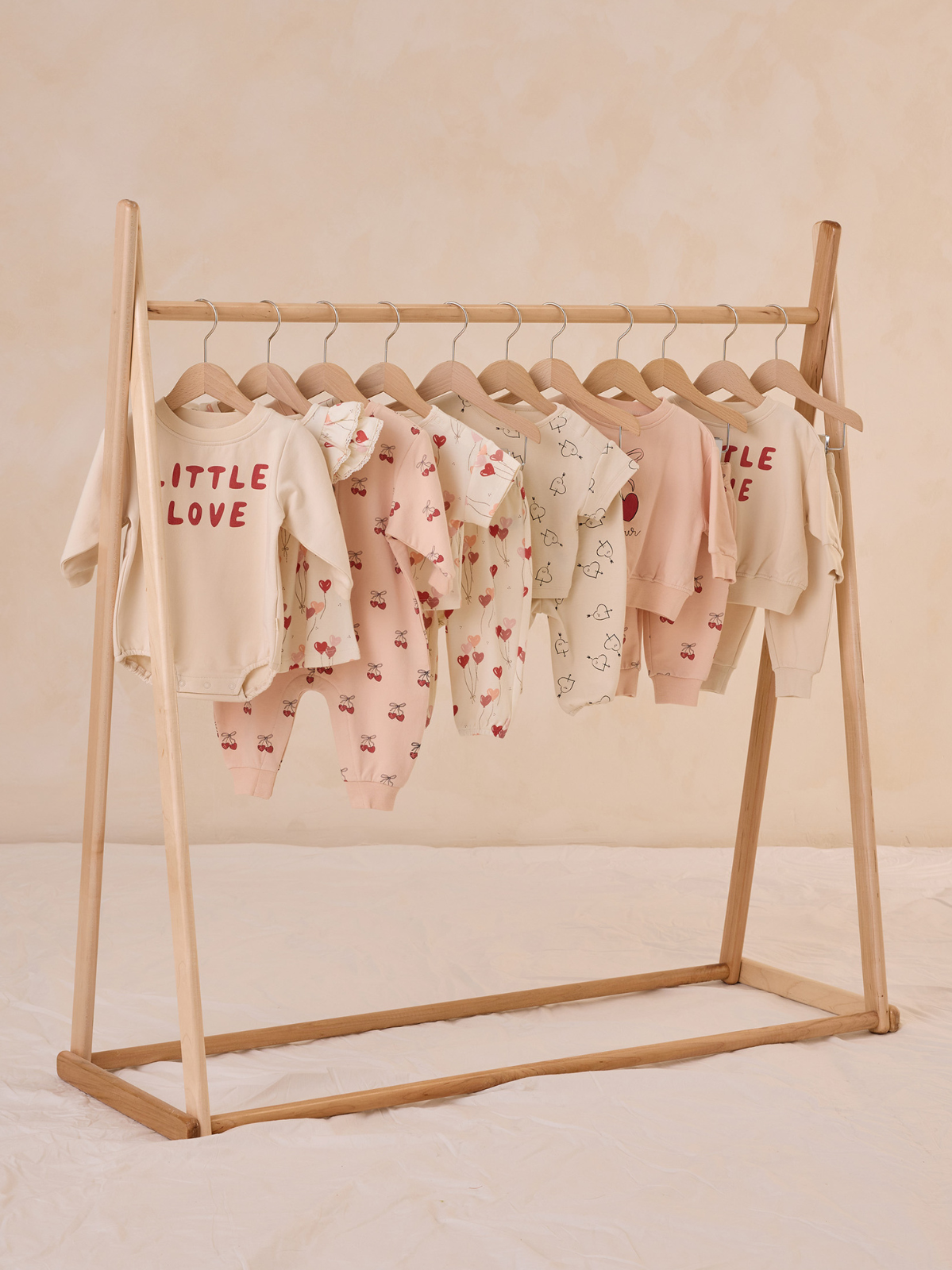 Light-colored baby clothes displayed on a wooden rack against a soft, neutral background.