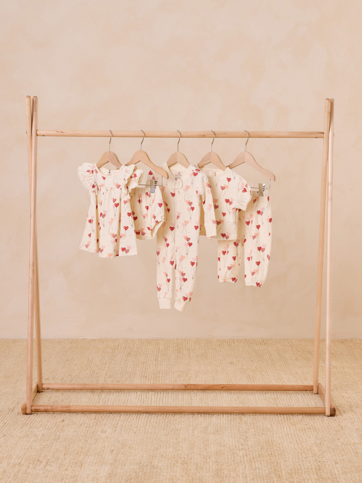 Children's clothing with heart patterns displayed on a wooden rack against a neutral background.