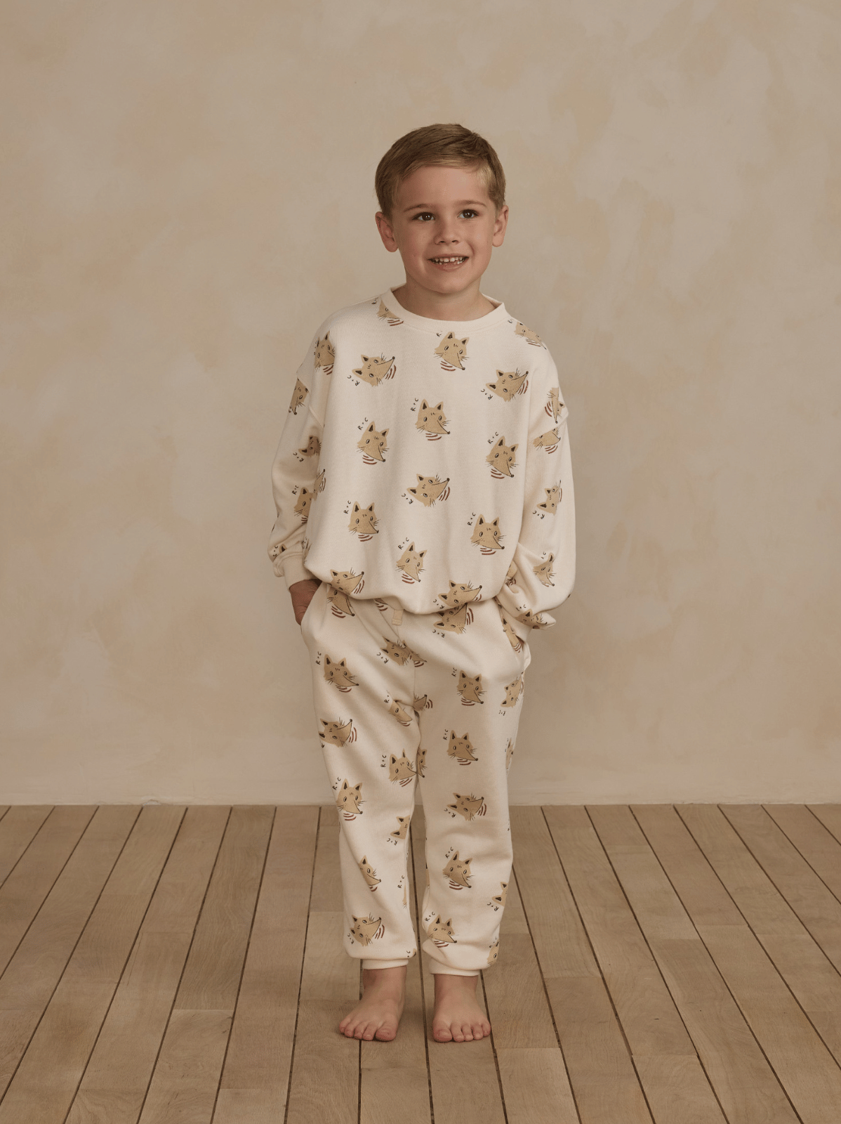 Smiling boy in cozy pajamas with animal print, standing on wooden floor against a light background.