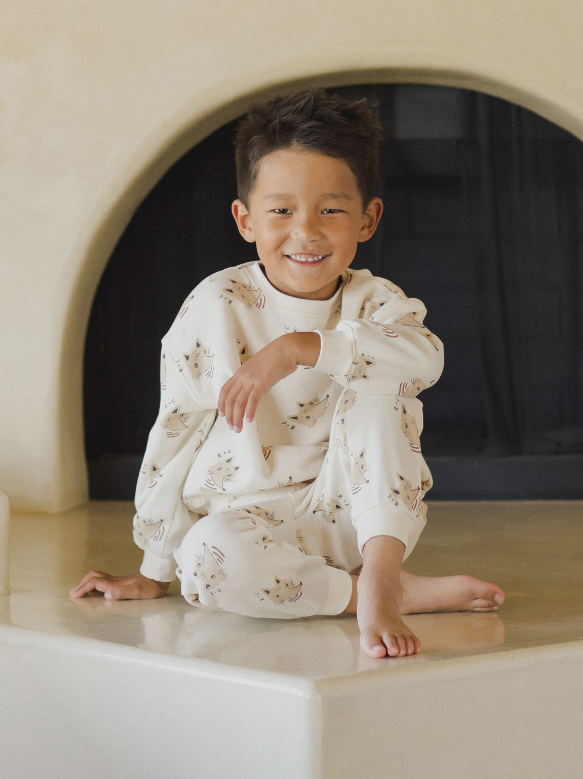 Smiling child in cat-themed pajamas sitting on a smooth surface. Warm, inviting background.