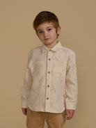 Child in a beige patterned button-up shirt poses against a light background.