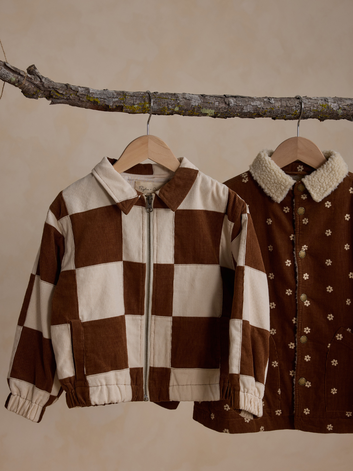 Two trendy brown jackets hanging from a twig: one checkered and the other with floral accents.