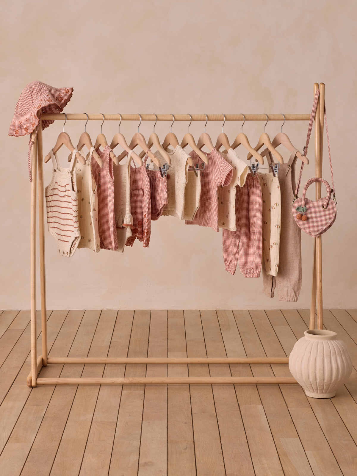 Children's clothing displayed on a wooden rack, featuring various styles in soft colors and a decorative bag.