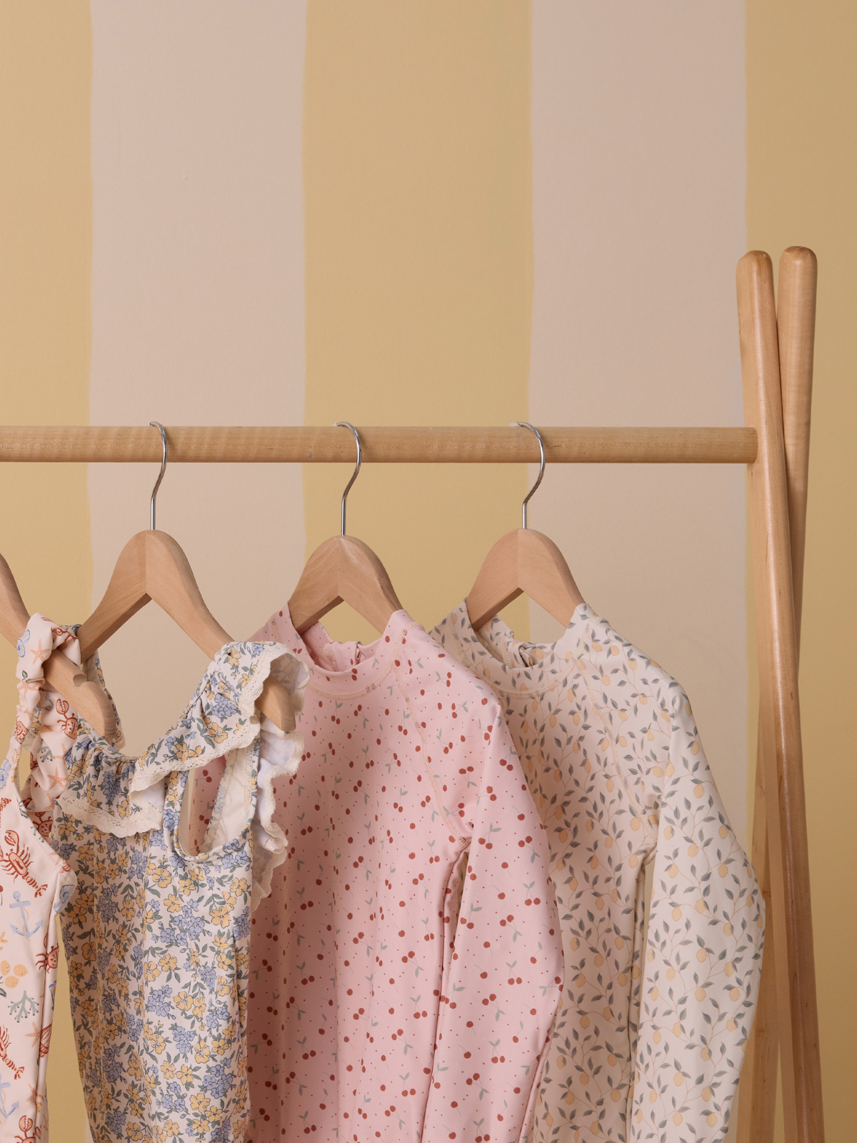 Colorful clothes hanging on wooden hangers against a soft yellow striped background.