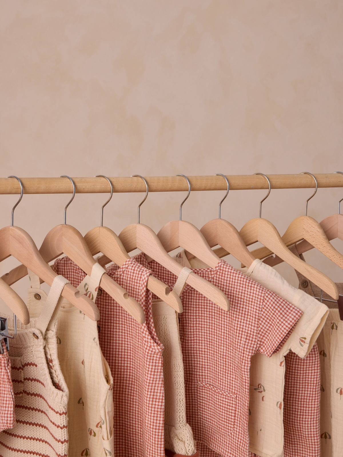 Hanging children's clothing in soft hues on wooden hangers against a neutral background.