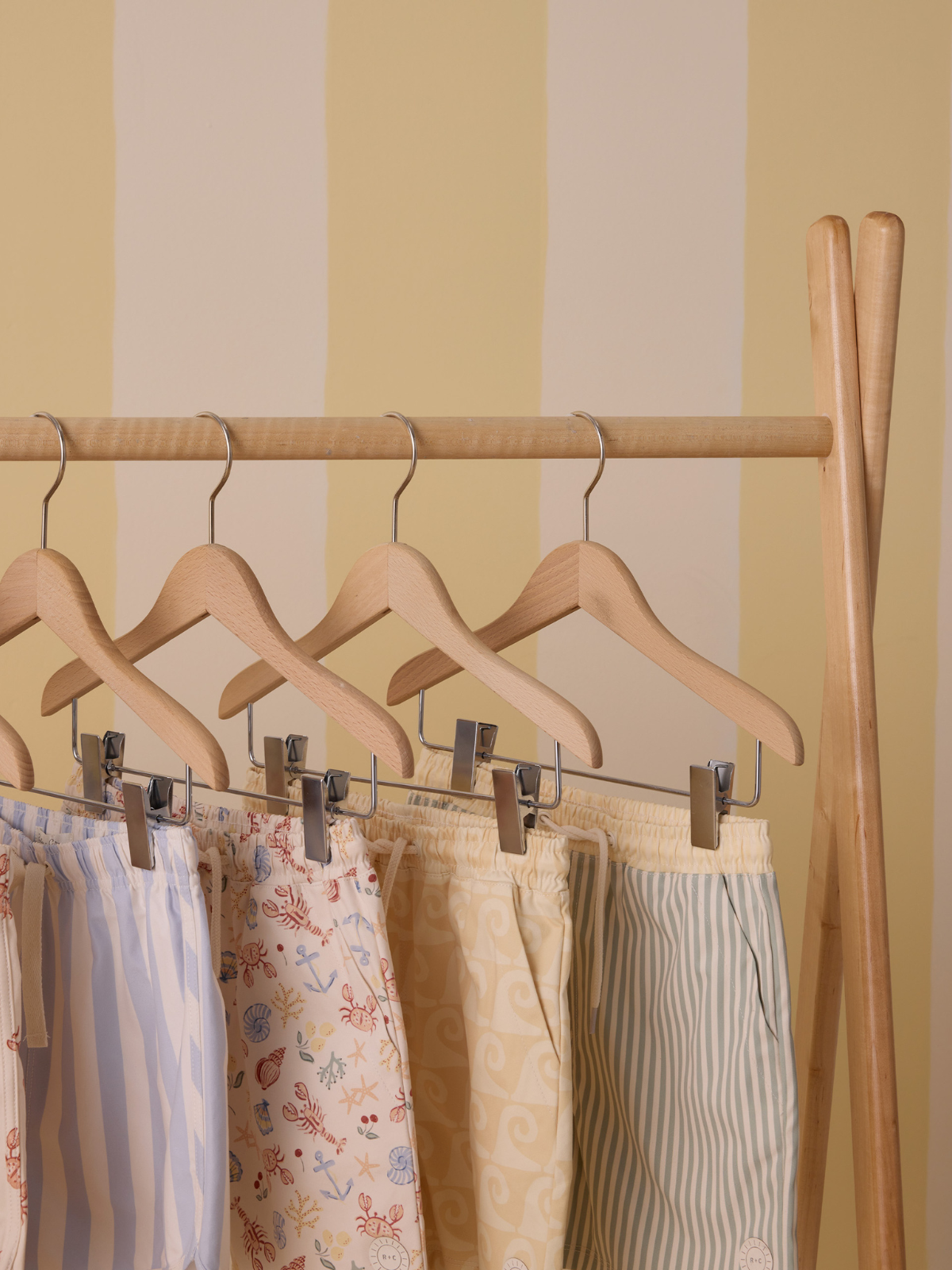 Colorful beach shorts hanging on wooden hangers against a soft yellow striped wall.