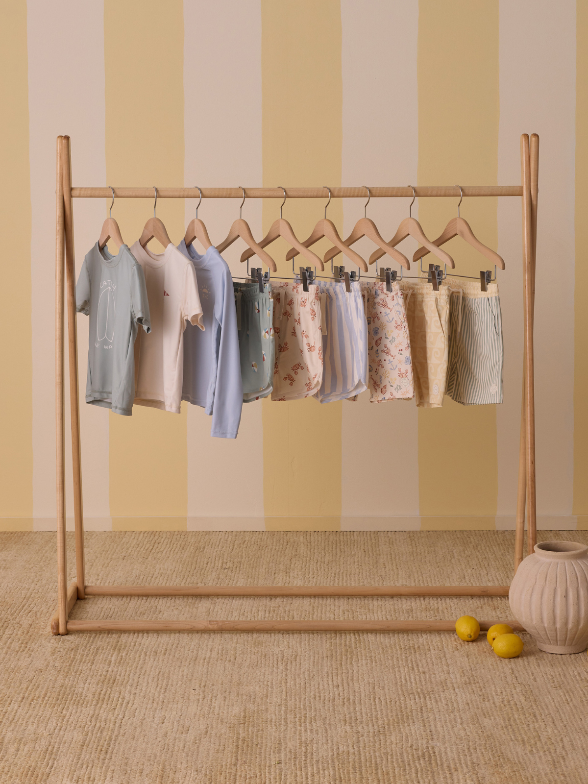Children's clothing displayed on a wooden rack with a soft yellow striped background.