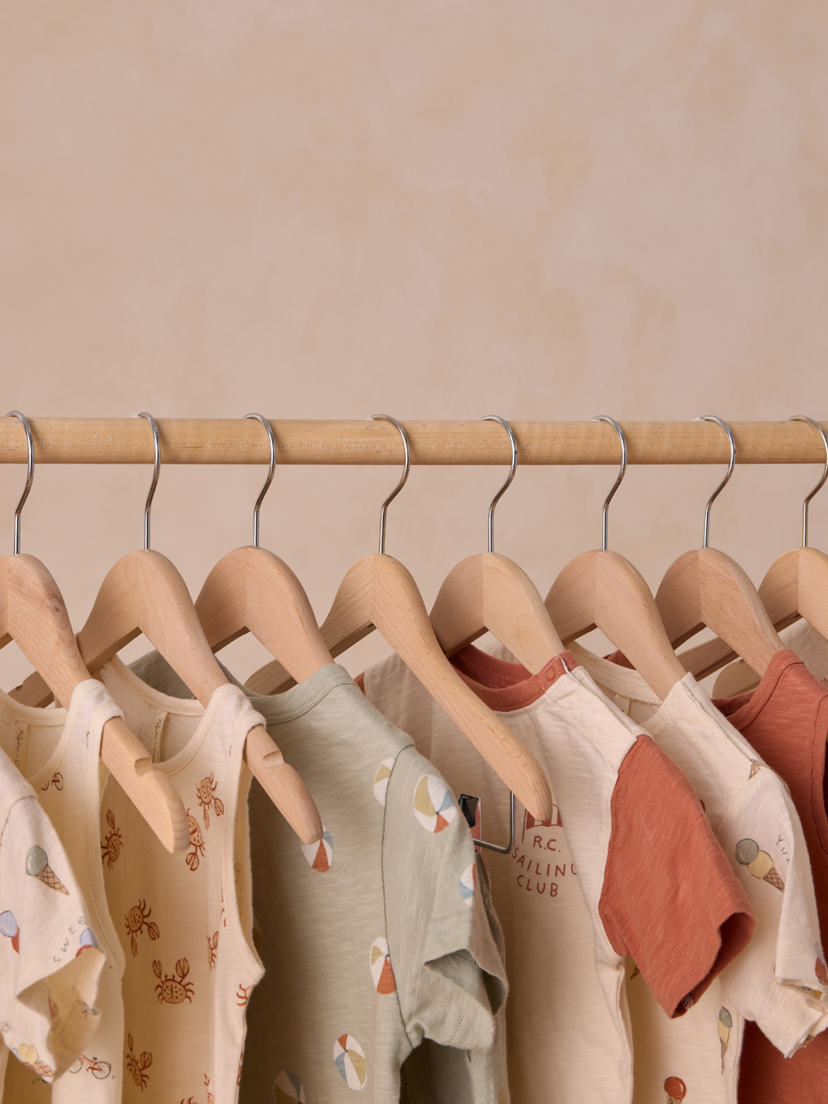 Assorted children’s shirts hanging on wooden hangers against a soft, neutral background.