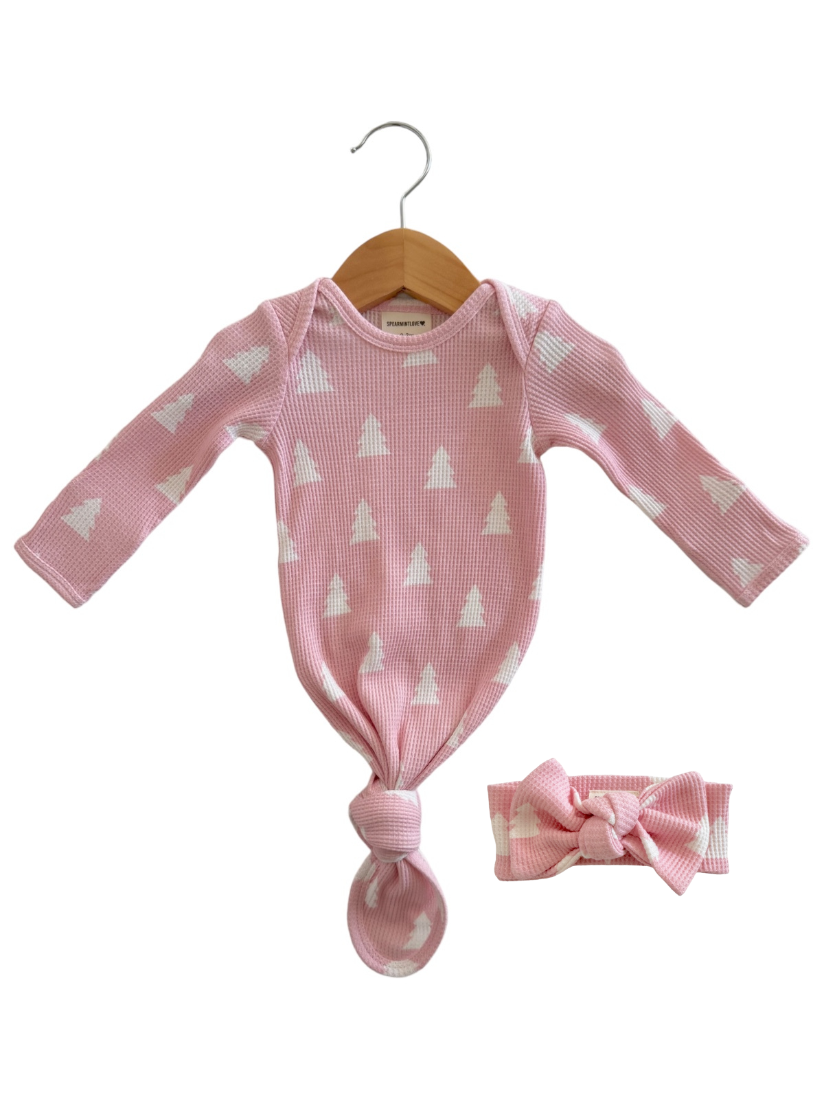 Pink baby outfit with long sleeves and knot detail, accompanied by a matching headband, hanging on a wooden hanger.