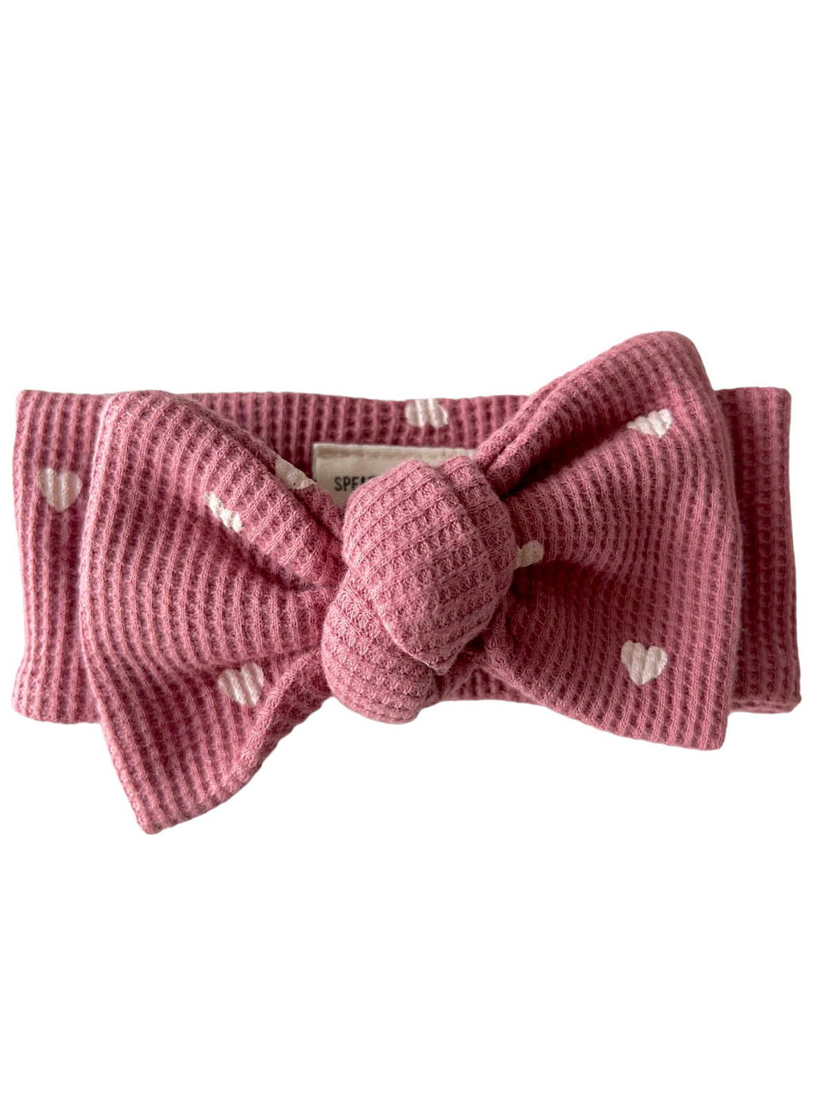 Light pink textured headband with a large bow and heart patterns. Ideal for stylish hair accessory.