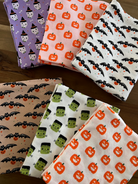 Colorful Halloween-themed fabric pieces featuring pumpkins, bats, and spooky characters arranged on a wooden surface.