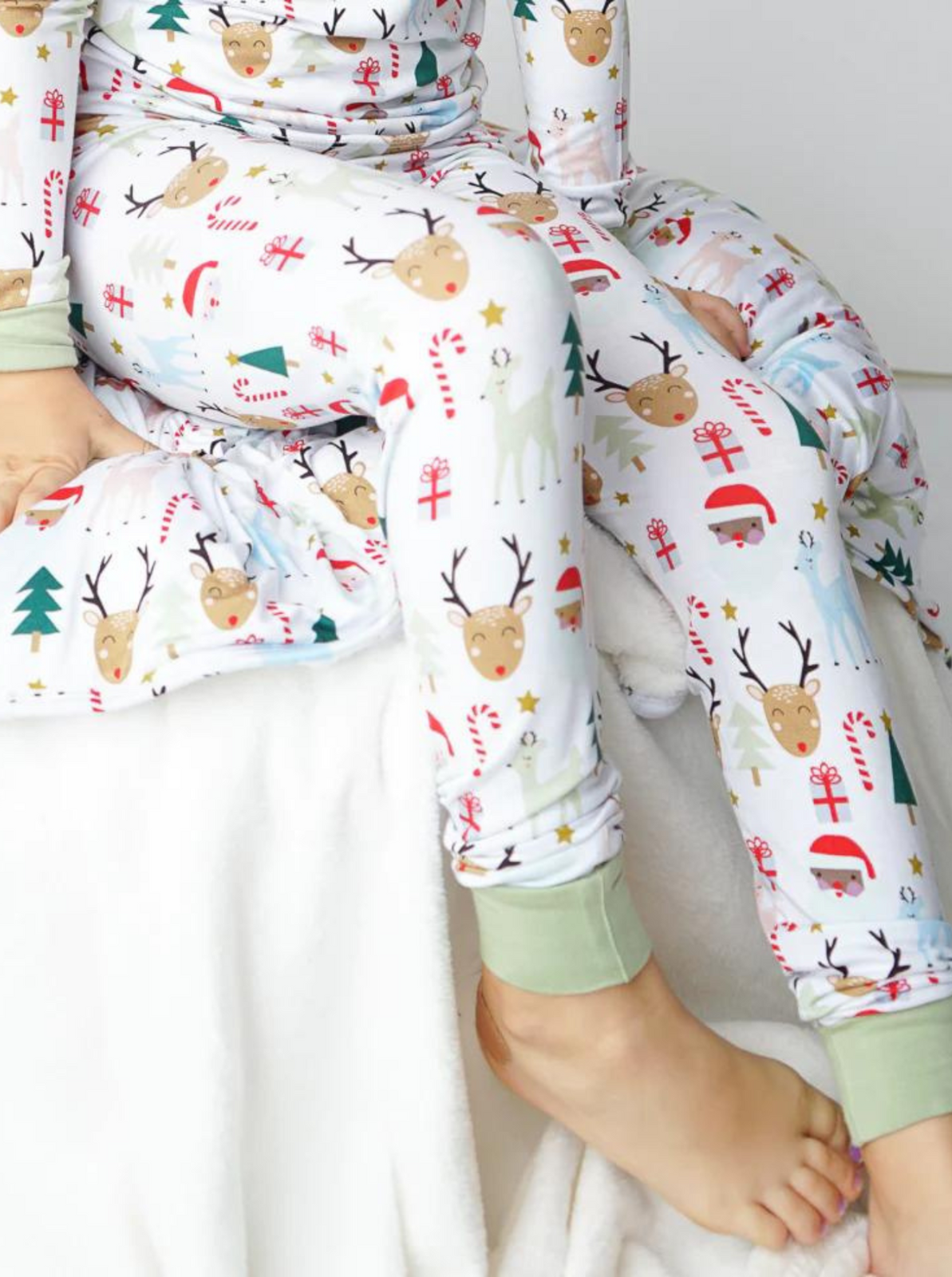 Child wearing festive pajamas with reindeer and holiday patterns, seated on a cozy blanket.