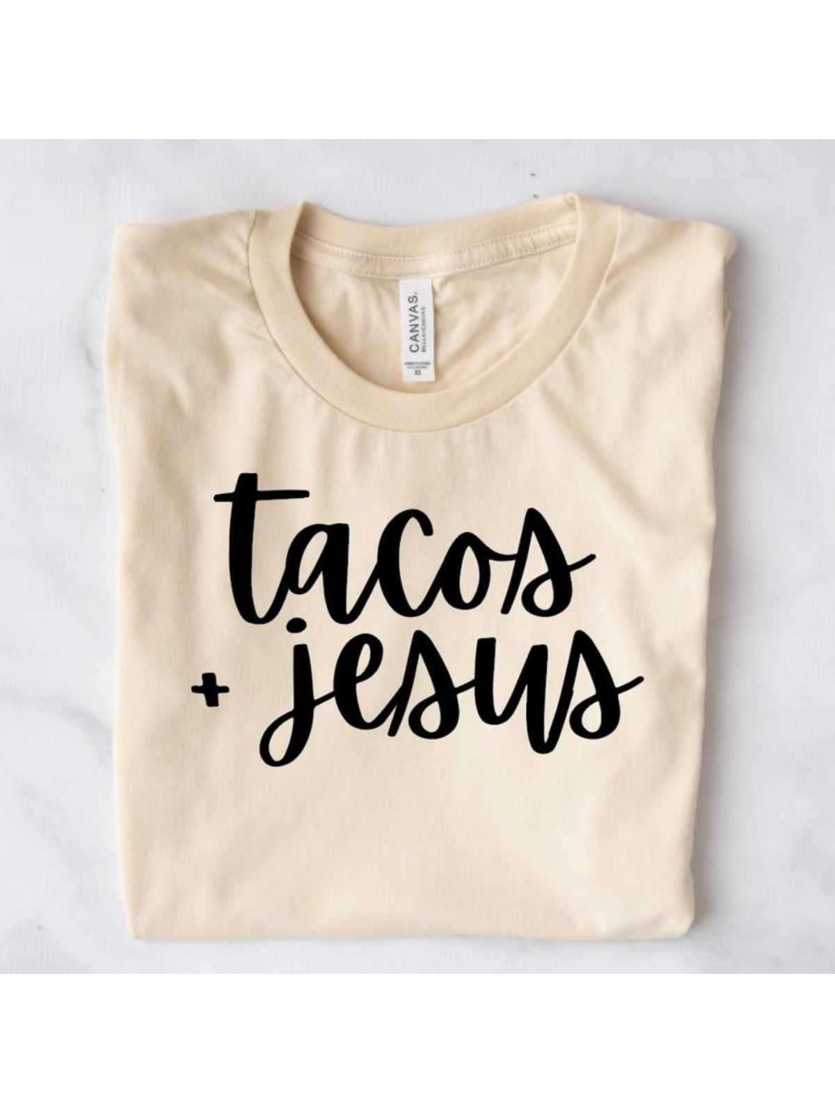 Light beige t-shirt featuring the text "tacos + Jesus" in bold black handwriting.