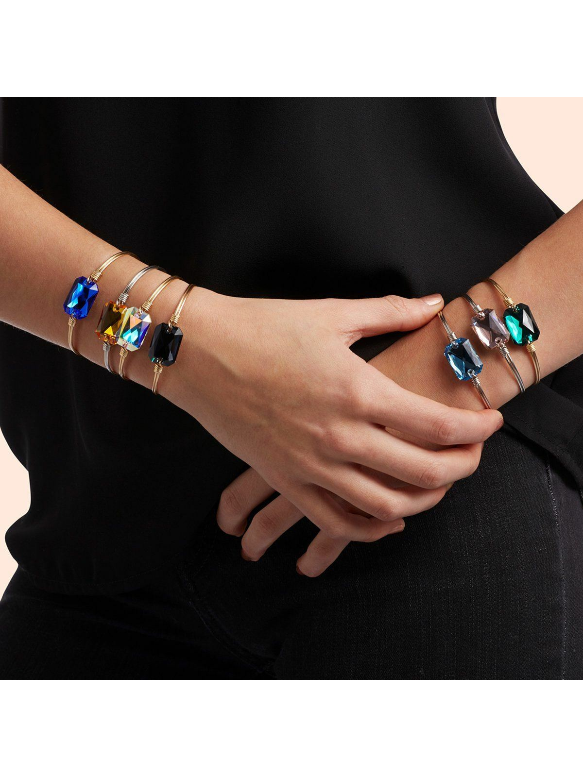 Model wearing multiple colorful bracelets on her wrist against a black background, showcasing elegant jewelry.