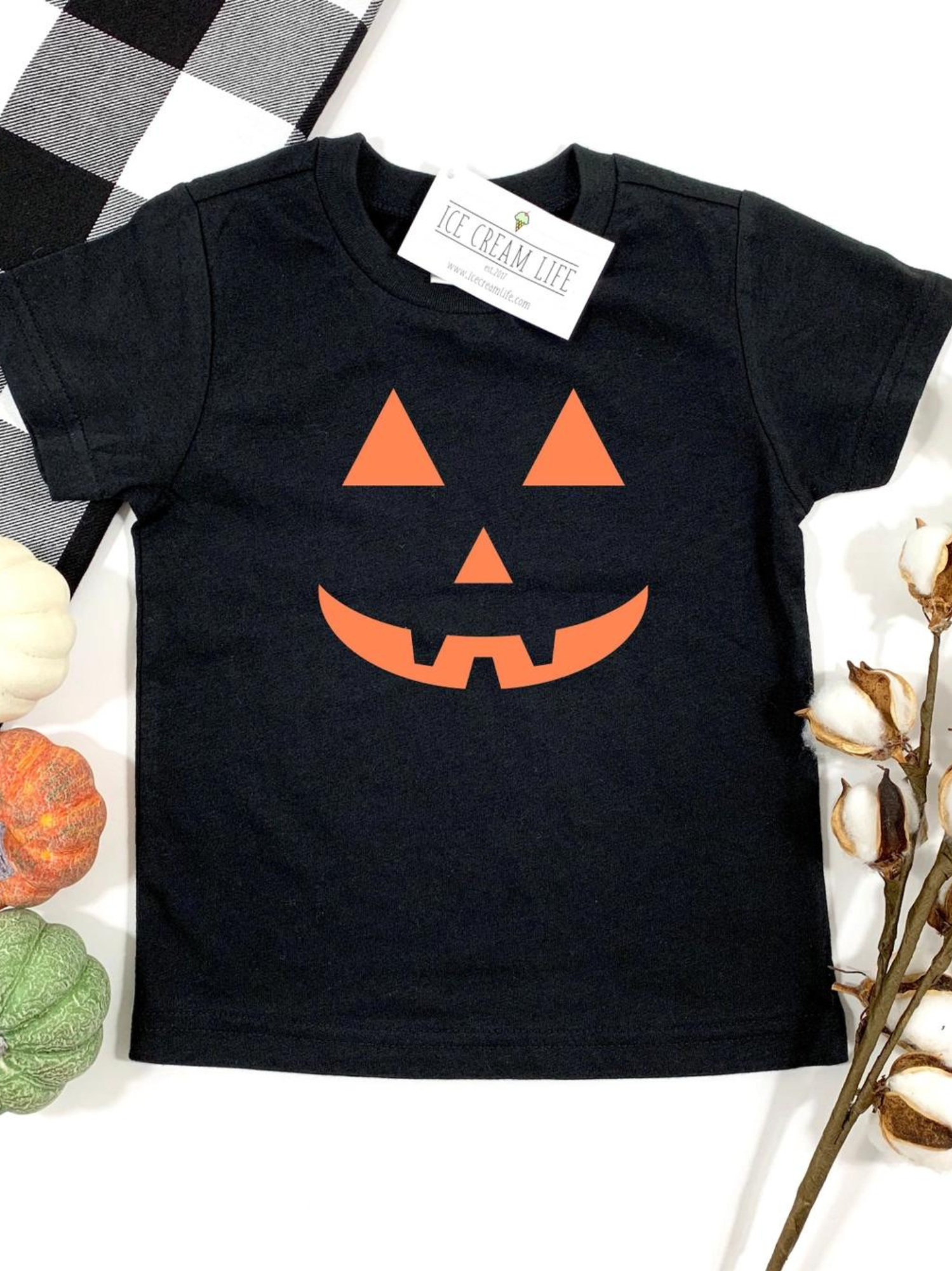 Black toddler t-shirt featuring an orange jack-o'-lantern design, surrounded by decorative pumpkins and cotton stems.