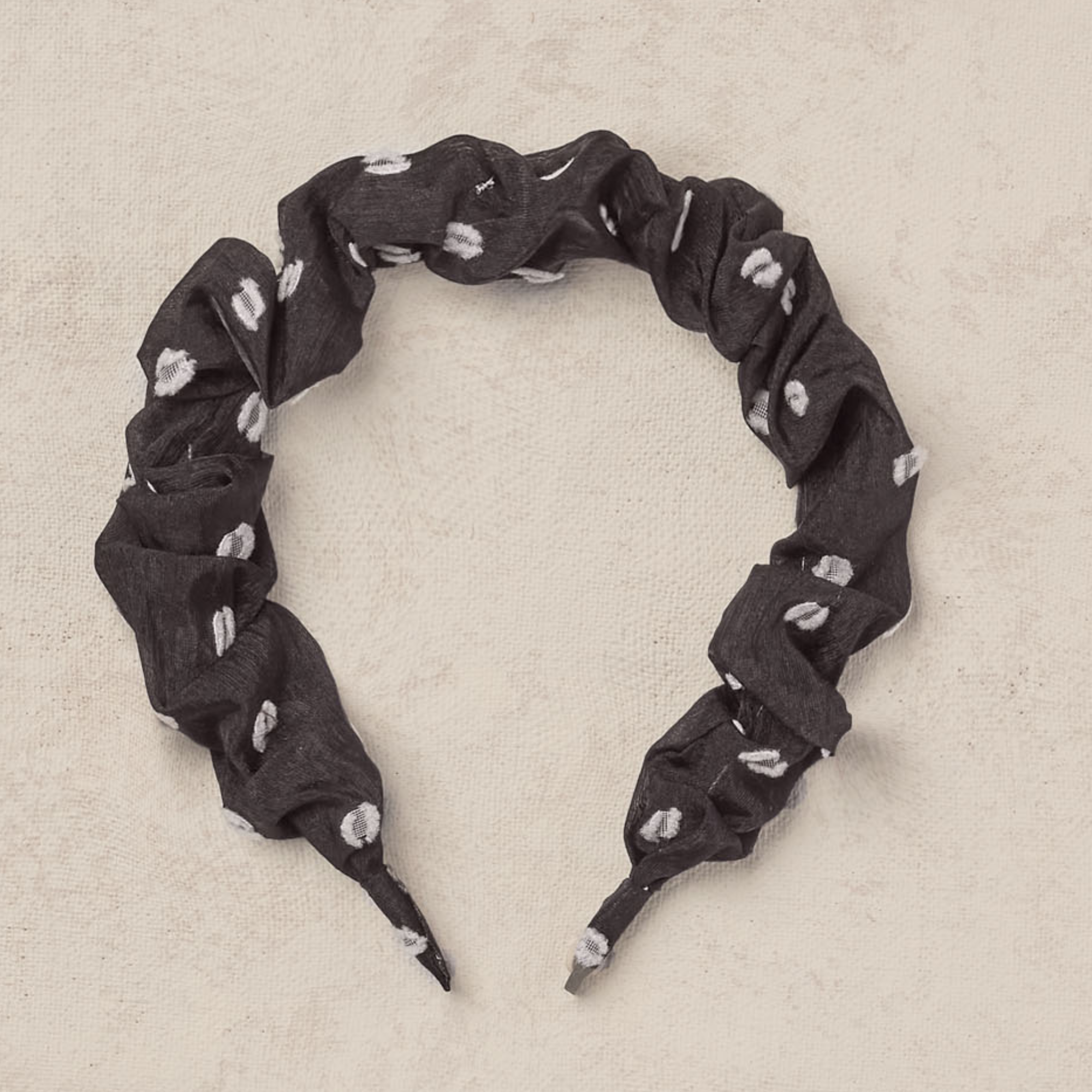 Black fabric headband with white polka dots, twisted design on a beige background.