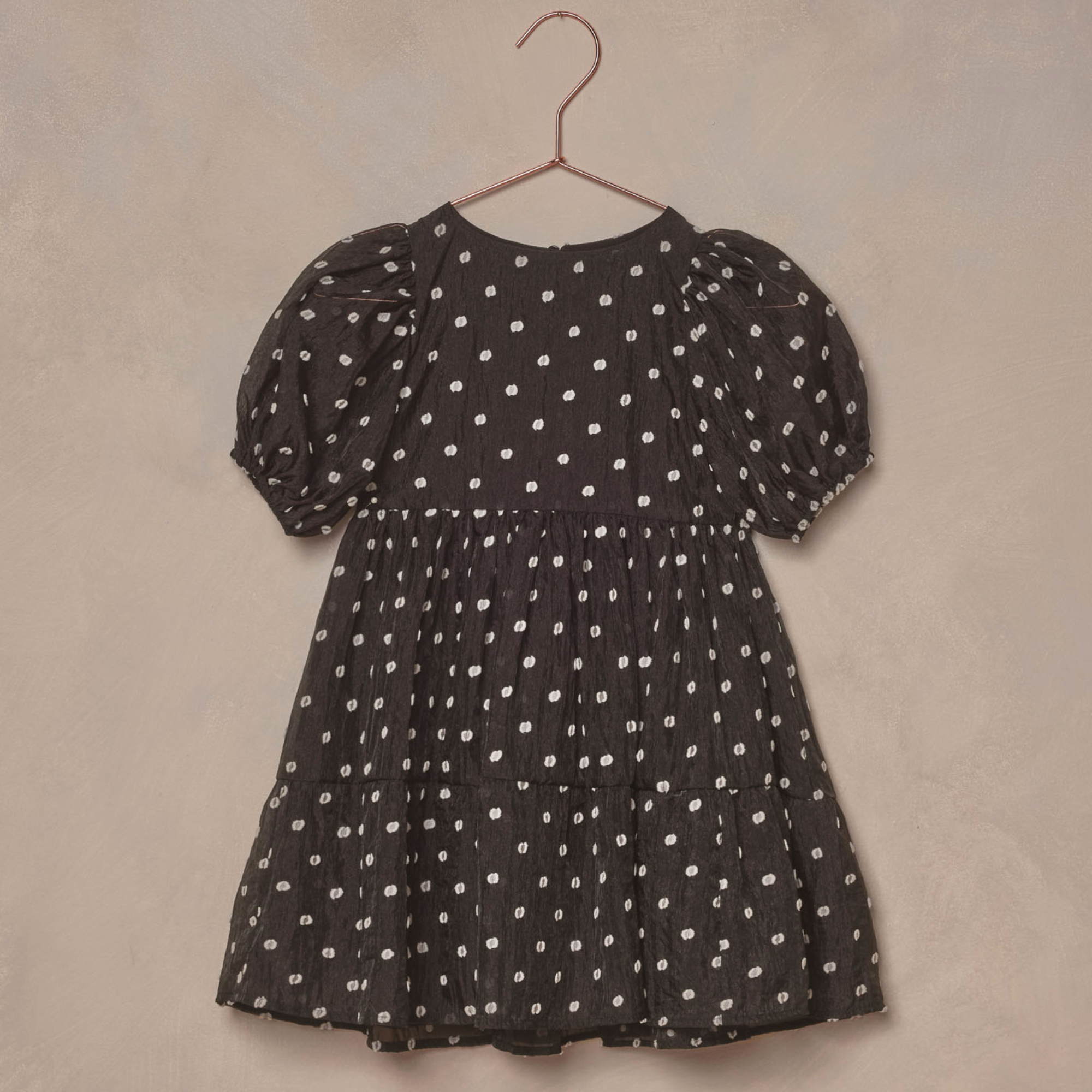 Black dress with white polka dots, featuring puff sleeves and a tiered design, hung on a copper-colored hook.
