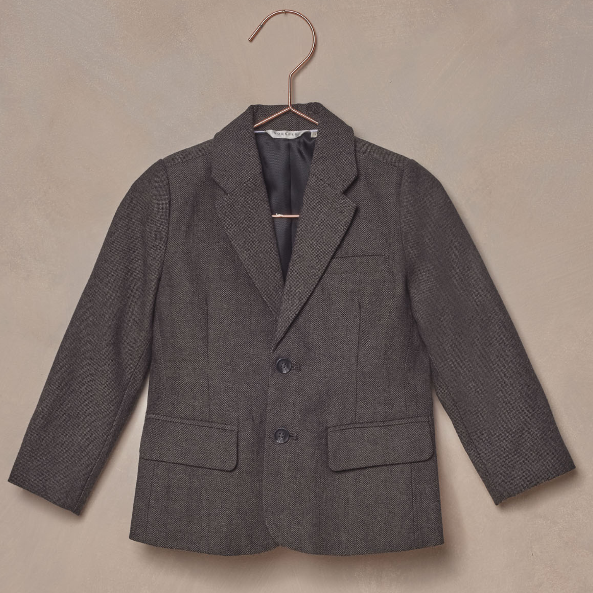 Gray children's blazer hanging on a rose gold hook against a textured background.
