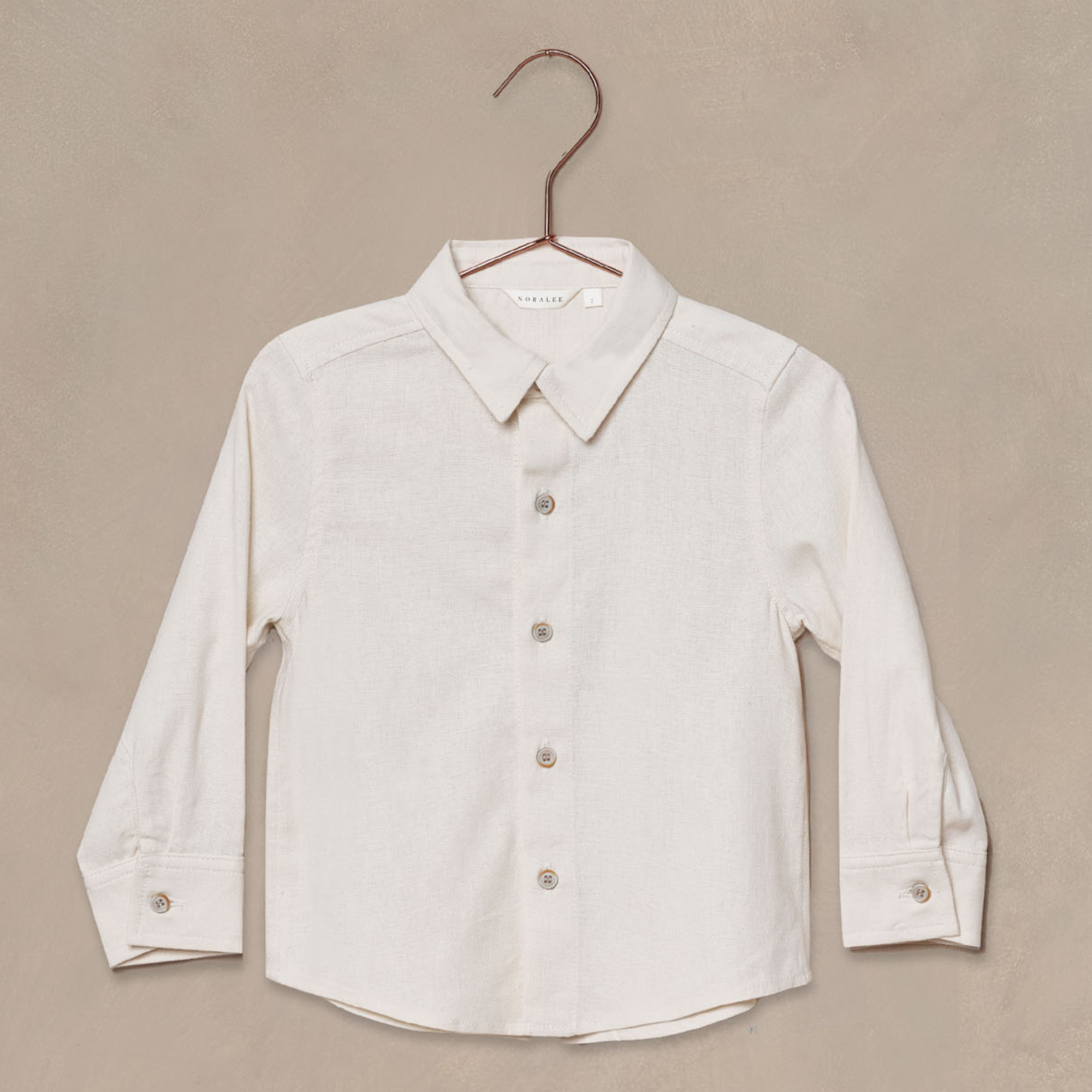 Light-colored children's button-up shirt displayed on a hanger against a textured background.