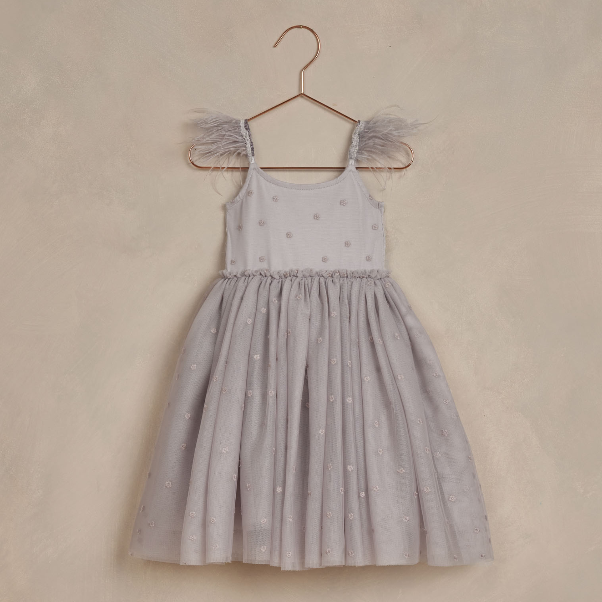 Gray dress with feathered straps and a twirl-ready skirt, hanging on a rose gold hanger against a soft background.