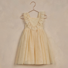 Light yellow dress with lace trim, hanging on a copper-colored hook against a textured background.