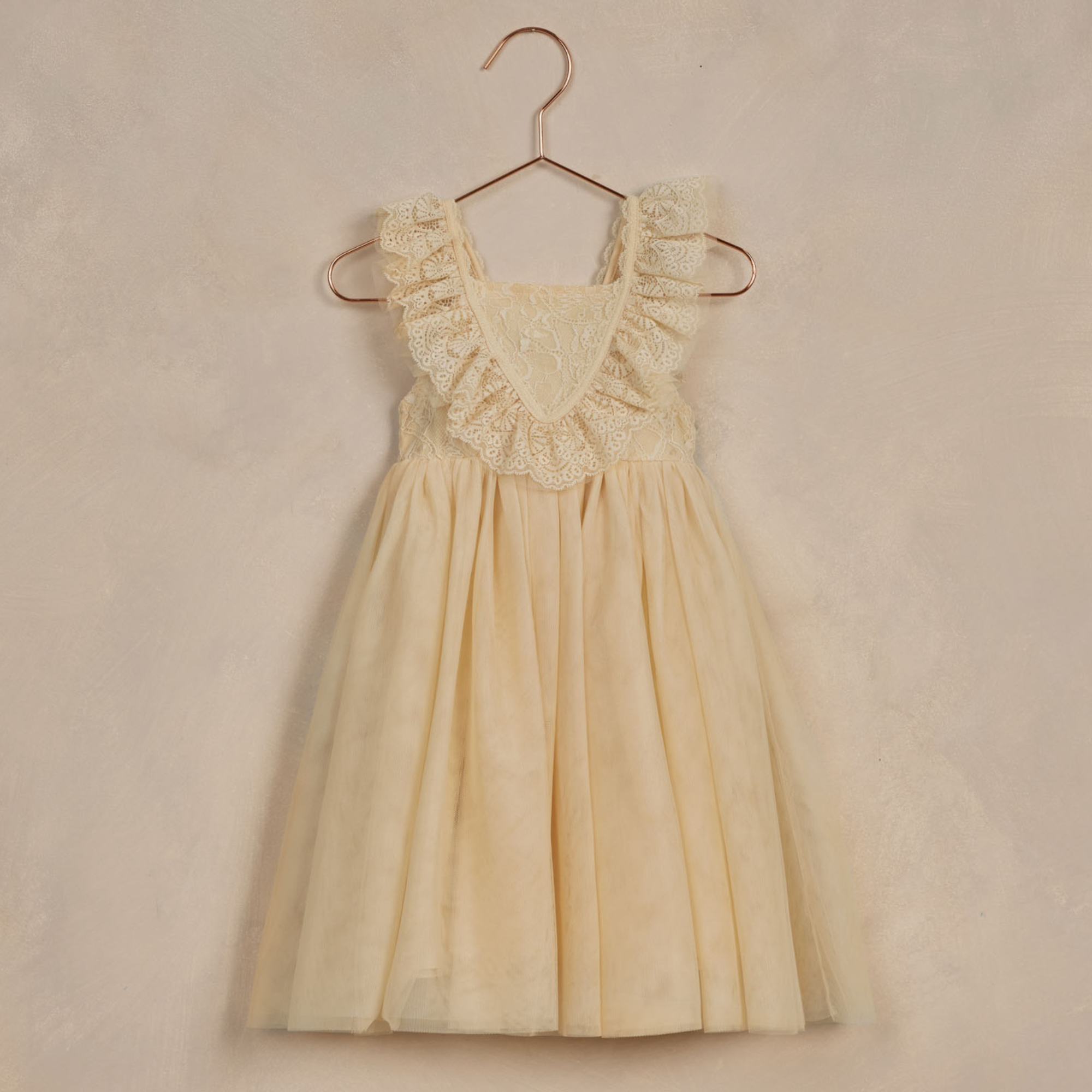 Light yellow dress with lace trim, hanging on a copper-colored hook against a textured background.