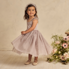 Girl in a pink dress spinning joyfully, surrounded by flowers and a soft, neutral background.