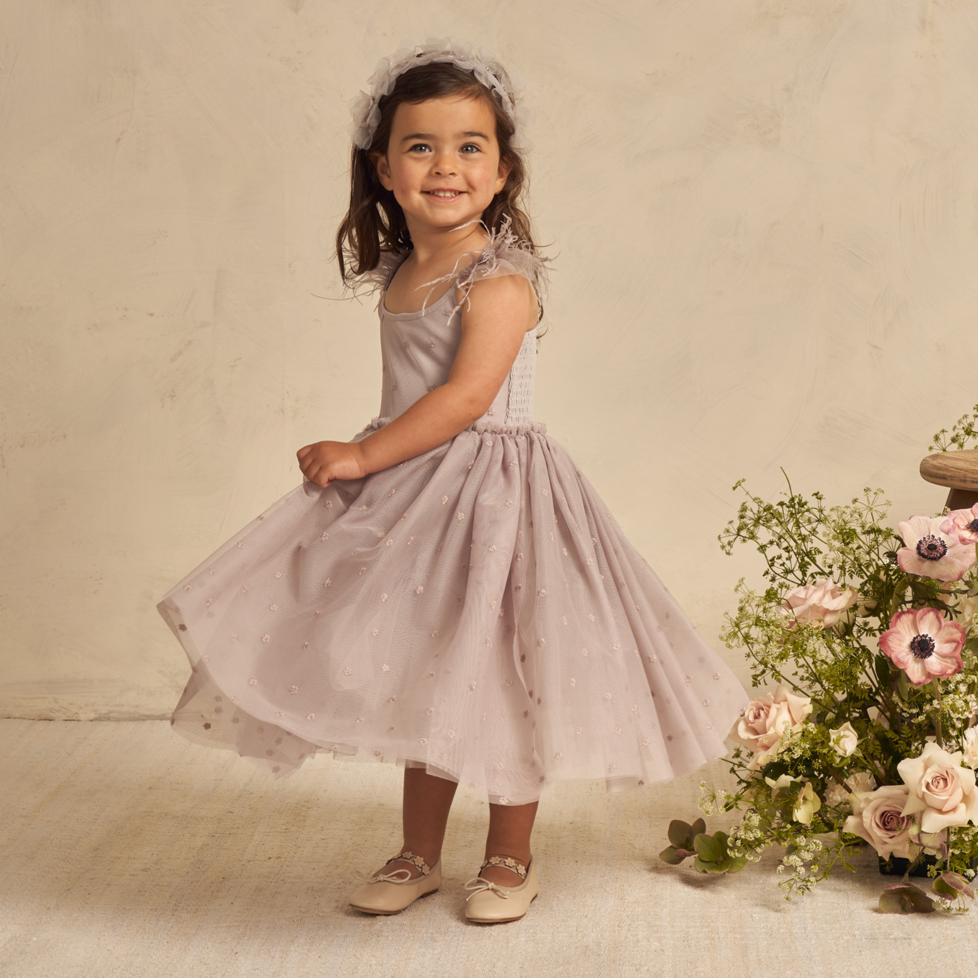 Girl in a pink dress spinning joyfully, surrounded by flowers and a soft, neutral background.