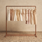 Group of vintage-style dresses hanging on a copper rack against a textured beige background.