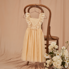 A cream-colored dress with lace detailing hangs on a wooden chair, surrounded by white flowers.