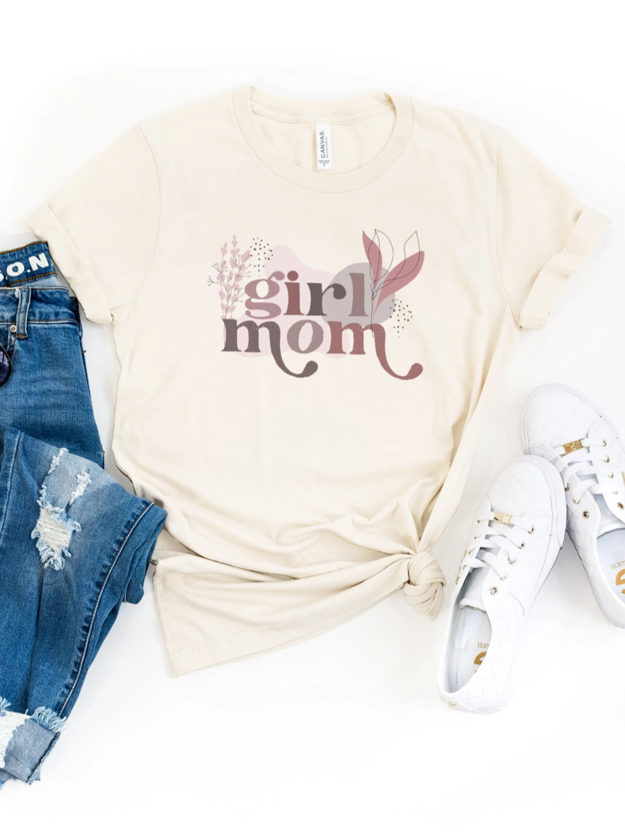 Beige t-shirt with "girl mom" graphic, denim jeans, and white sneakers arranged aesthetically on a white background.