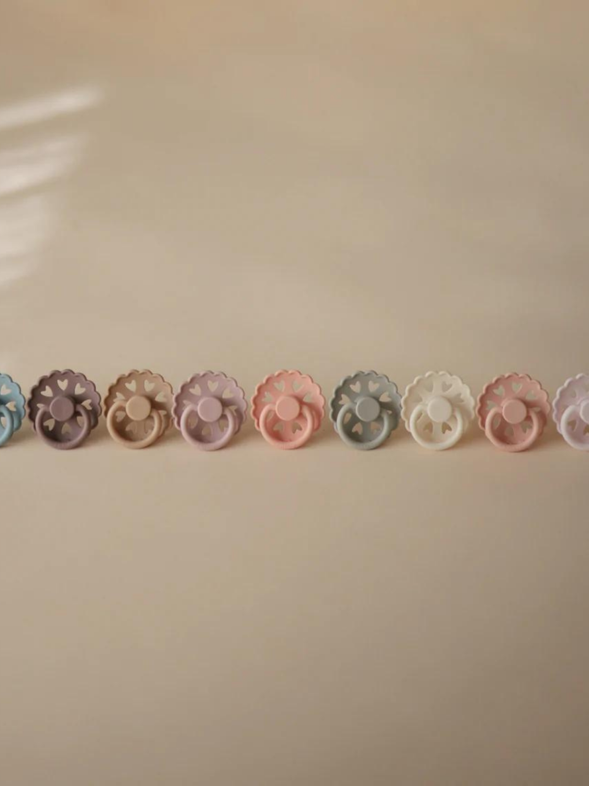 A row of colorful, flower-shaped pacifiers on a beige background, showcasing pastel shades and playful designs.